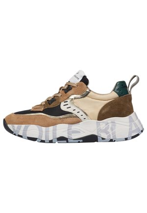 Zapatillas de hombre con una mezcla de ante marrón y materiales sintéticos crema. Cuenta con acentos negros, suela texturizada y una lengüeta trasera verde.