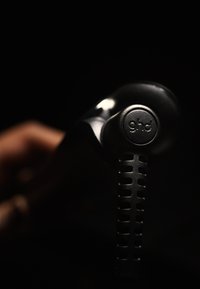 Schwarzer Haarglätter mit einer glatten, glänzenden Oberfläche. Verfügt über einen strukturierten Griff mit Aussparungen und einem runden Logo am Griff.