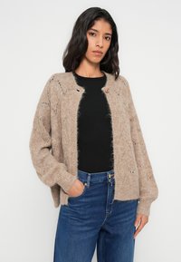 Μπεζ πλεκτή ζακέτα με υφή αφράτη και ανάγλυφη. Διαθέτει στρογγυλή λαιμόκοψη, κούμπωμα με κουμπιά και φαρδιά, μακριά μανίκια.