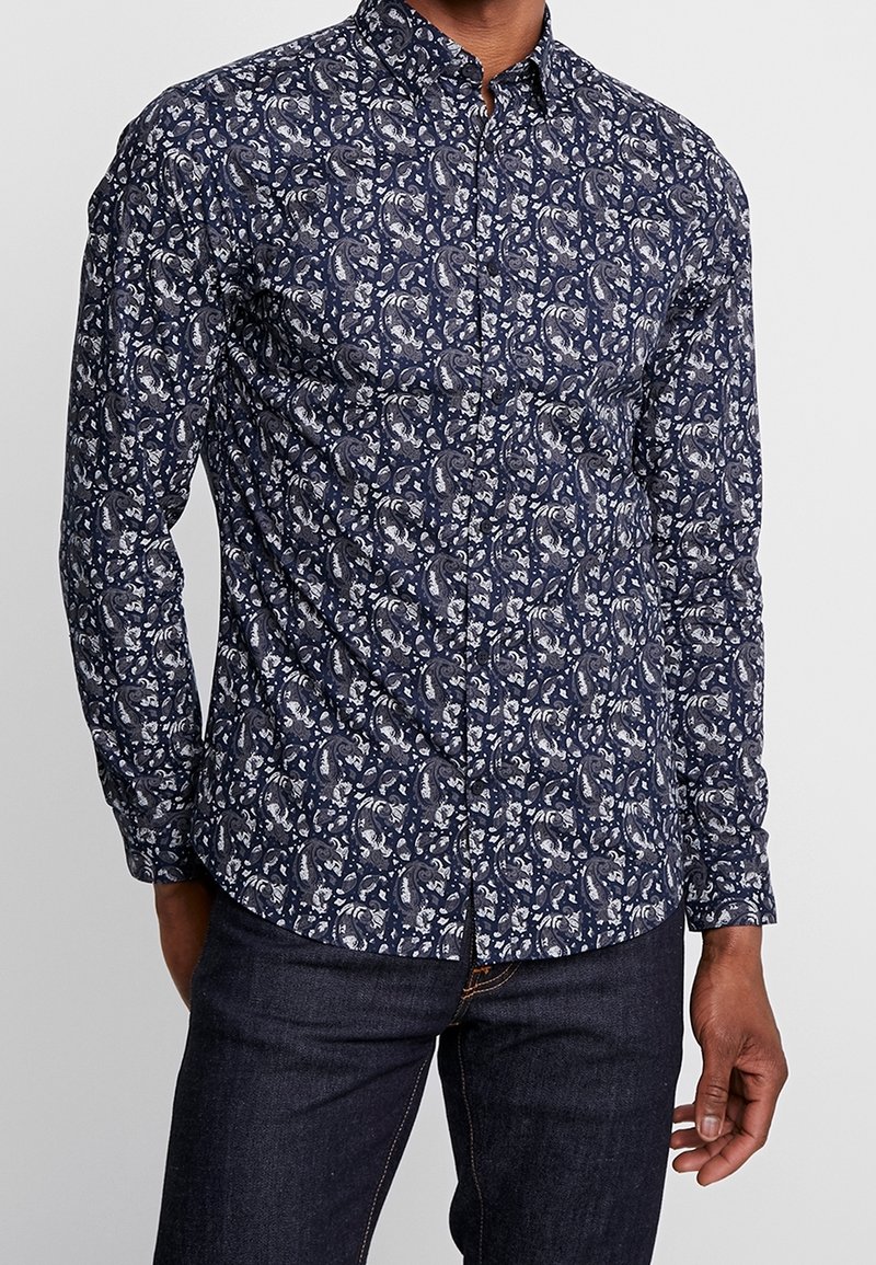 Camisa de botones azul marino con un patrón floral paisley en blanco, de mangas largas y con un cuello clásico. Fabricada en una tela suave y texturizada.