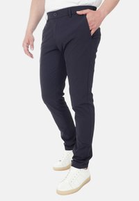 Pantaloni navy con una vestibilità slim, realizzati in tessuto leggero. Presentano quattro tasche e una chiusura frontale con bottone, abbinati a sneakers bianche.