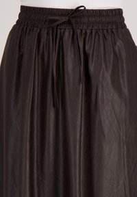 Zwarte, lichte rok met een elastische tailleband en een verstelbaar trekkoord. Heeft een gladde, iets gekreukte textuur.