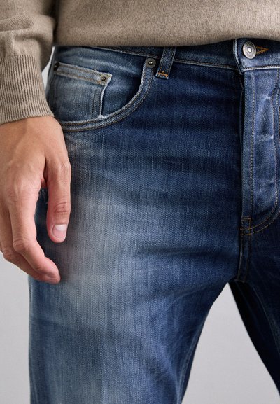 Jeans in denim blu scuro con leggere scoloriture, caratterizzati da una vestibilità slim, un classico design a cinque tasche e dettagli in metallo.