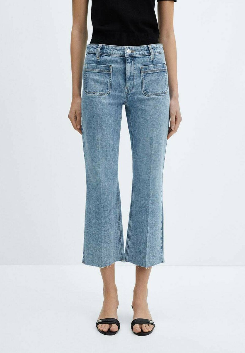 Jeans de mezclilla de corte acampanado en azul claro con dobladillo sin rematar y bolsillos delanteros, combinados con sandalias negras. La tela parece suave con una ligera textura.