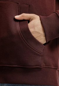 Burgundowa bluza z kieszenią z przodu, ściągaczem na rękawach i dole, miękka tekstura oraz luźny krój dla komfortu.