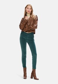 Brown faux leather cropped jacket, green corduroy slim-fit pants, and brown heeled ankle boots. Smooth texture and fitted design.