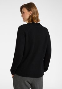 Czarny sweter z prążkowanej dzianiny z okrągłym dekoltem, z długimi rękawami i lekko luźnym krojem, zestawiony z szarymi spodniami, pokazany z tyłu.