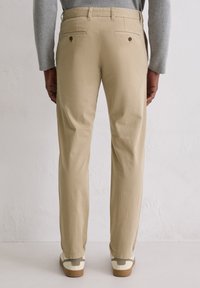 Khaki chinos with a straight fit, cotton material, two back pockets with button closures, paired with white and green sneakers.