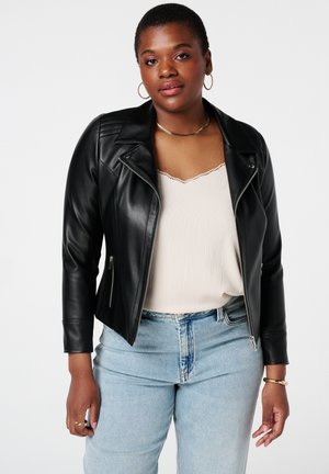Veste de biker en simili cuir noir avec fermeture éclair à l'avant, détails matelassés sur les épaules, associée avec un haut beige à côtes et un jean bleu clair.