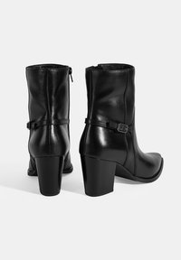 Bottines en cuir noir avec fermeture éclair, bout carré et talon bloc. Présentent une petite sangle avec un détail de boucle.