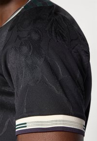 Must have musta T-särk musta kangast, tekstuurse lillemustriga, lühikeste varrukatega ja kontrastse triibulise soonikuga kaelusega, millel on elastsed detailid.