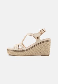 Sandalia cuña en beige con tiras de textil trenzadas, hebilla ajustable en el tobillo y plataforma texturizada similar a yute con detalles cosidos.