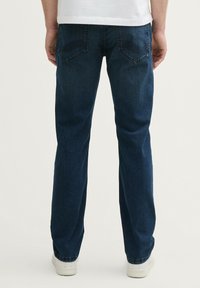 Jeans de mezclilla azul marino con un diseño de pierna recta, que presentan bolsillos traseros con detalles de costura sutiles, llevados con zapatillas blancas.