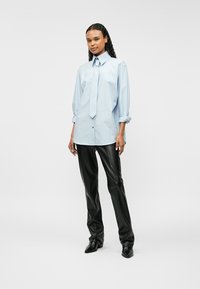 Ανοιχτό μπλε φαρδύ πουκάμισο με κολάρο και γραβάτα, σε συνδυασμό με μαύρο δερμάτινο παντελόνι και παπούτσια με μυτερή μύτη. Λείος ύφασμα, χαλαρή εφαρμογή.