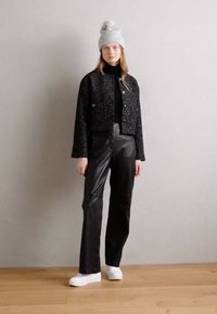 Giacca nera corta in tessuto testurizzato, dolcevita nera, pantaloni in pelle a vita alta e sneakers bianche con plateau. Berretto grigio a maglia con pompon.