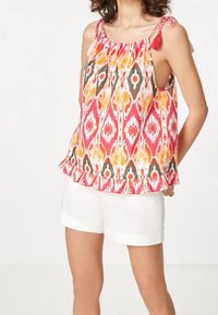 Haut sans manches avec un motif ikat multicolore, doté d'un ourlet festonné et de liens avec des pompons roses sur les bretelles.