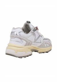 Scarpa sportiva in rete bianca con accenti grigi, suola in gomma spessa e dettagli testurizzati. Presenta un anello in tessuto e un design con lacci.