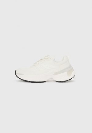 Weiße sportliche Sneaker mit einer strukturierten Oberseite, Schnürverschluss und einer klobigen Sohle, die eine schwarze Gummisohle und durchsichtige Akzente aufweist.