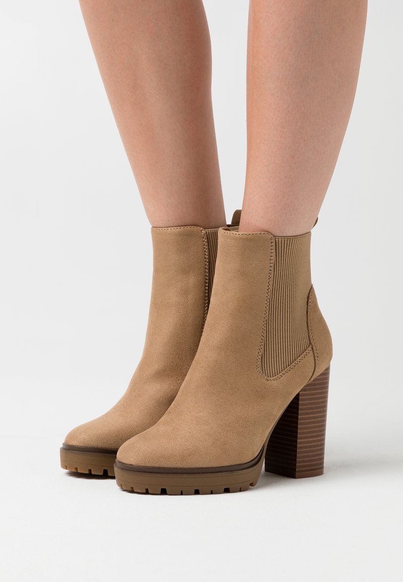 Bottes de cheville en suede tan avec des panneaux latéraux côtelés et un talon épais empilé. La semelle présente des rainures de traction pour une meilleure adhérence.