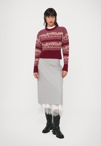 Maroon knitted sweater with light patterns and ribbed hem, paired with a gray skirt featuring a lace trim. Black knee-high boots.