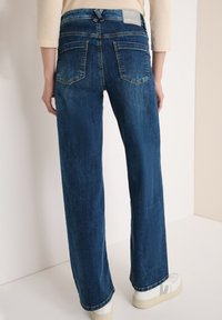 Wijd gesneden blauwe denim jeans met een donkere wassing, voorzien van twee achterzakken en een merklabel op de taille. De stof heeft een licht gestructureerde afwerking.
