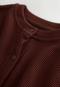 Bordový pletený sveter s rebrovaným dizajnom, s okrúhlym výstrihom a dvoma okrúhlymi hnedými gombíkmi vpredu.
