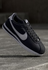Černé kožené tenisky s šedými akcenty, texturovaným povrchem, bílou mezipodešví a podrážkou s cik-cak vzorem. Vybaveny výrazným logem swoosh.