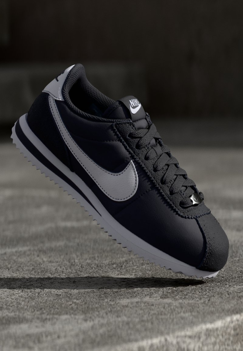 Černé kožené tenisky s šedými akcenty, texturovaným povrchem, bílou mezipodešví a podrážkou s cik-cak vzorem. Vybaveny výrazným logem swoosh.