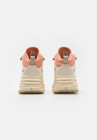 Sneakers with a peach upper and cream lower sections, featuring a textured fabric, padded collar, and reflective hardware accents.