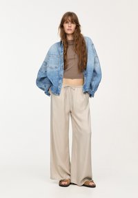 Ljusblå denim oversized jacka med framfickor, brun kort topp och beige vida byxor. Bruna sandaler med remmar.
