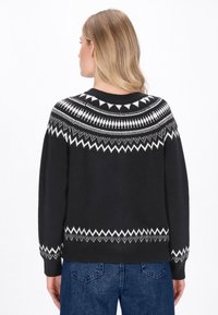 Fekete kötött pulóver fehér geometrikus mintával és cikk-cakk mintázattal a galléron és az alján. Laza fazonú, hosszú ujjú.