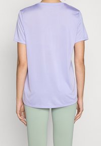 Camisa de manga corta en color púrpura claro, hecha de un tejido suave, con un escote redondo y un corte ligeramente relajado, combinada con leggings de color verde claro.
