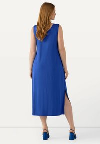 Abito maxi blu senza maniche con spacchi laterali, tessuto morbido e una vestibilità rilassata. Abbinato a sandali blu con tacco a blocco.