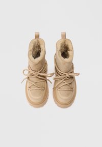 Καστανά σουέτ μποτάκια με επένδυση από συνθετική γούνα, στρογγυλή μύτη, χοντρή ελαστική σόλα και λεπτά κορδόνια. Διαθέτουν χρυσές λεπτομέρειες και χερούλι στην πίσω πλευρά.