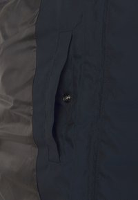 Granatowa kurtka z gładkiej, teksturowanej tkaniny. Posiada kieszeń z zapięciem na guzik i elegancki design. Lekka i odporna na wodę.