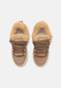 Baskets beige avec de larges lacets marron et une doublure en fourrure légère beige clair, vues de dessus sur un fond blanc.