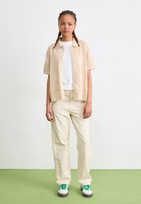 Beige knit short-sleeve shirt with a textured pattern, white t-shirt underneath, cream wide-leg pants, and green-accented sneakers.