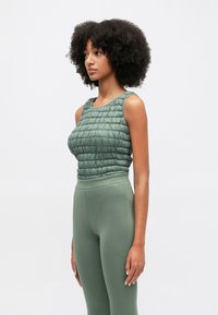 Πράσινη καπιτονέ αμάνικη μπλούζα με υφή στην επιφάνεια και φαρδιές τιράντες, συνδυασμένη με εφαρμοστά πράσινα κολάν, και τα δύο φτιαγμένα από ελαστικό ύφασμα.