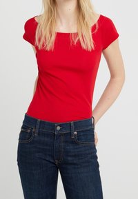 Röd kortärmad figurnära topp i mjuk bomull, kombinerad med mörkblå denimjeans med klassisk femfickdesign och kontrasterande sömmar.