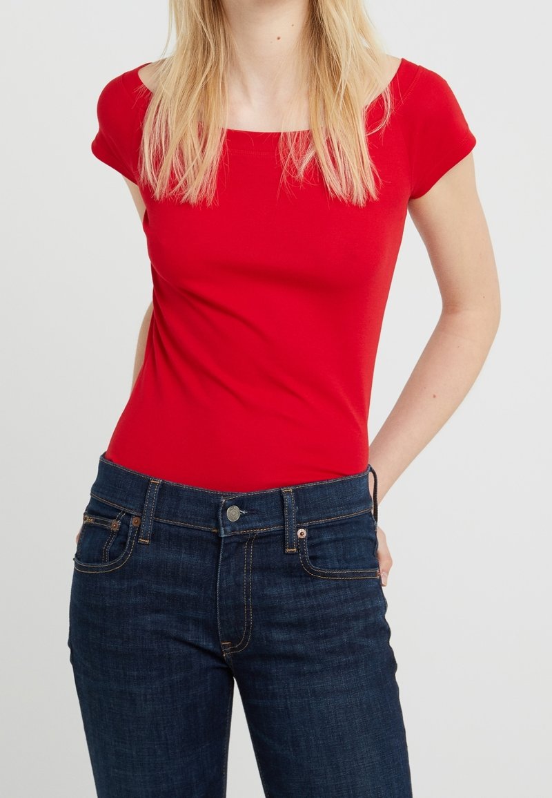 Röd kortärmad figurnära topp i mjuk bomull, kombinerad med mörkblå denimjeans med klassisk femfickdesign och kontrasterande sömmar.