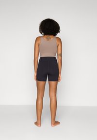 Top court sans manches marron associé à un short noir taille haute. Tissu lisse, design ajusté et détails de couture minimaux.