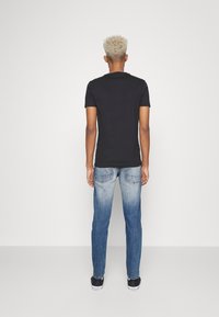 Camiseta negra de manga corta combinada con vaqueros azul claro, con un diseño desgastado, bolsillos estándar y zapatillas negras. Look limpio y casual.