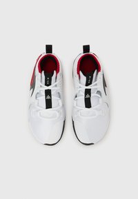 Λευκά αθλητικά παπούτσια με ανώτερο μέρος από διαπνέον πλέγμα, μαύρ ες λεπτομέρειες, κόκκινη εσωτερική επένδυση και αντίθετη υφή στη σόλα.