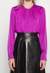 Fuchsia blus med veckad halsringning och långa ärmar, parat med en svart läderkjol med ett bälte med kedjedetaljer.