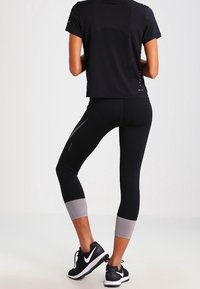 Musta urheilu toppi ja capri leggingsit harmailla yksityiskohdilla. Leggingsit ovat tyylikkään muotoilun ja tiukan istuvuuden omaavat, sopivat aktiiviseen käyttöön.