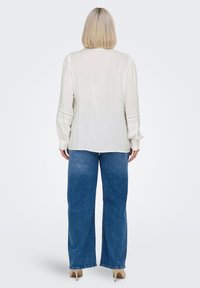 Long-sleeve, cream blouse with a subtle polka dot pattern, paired with high-waisted, wide-leg blue jeans. Soft fabric and relaxed fit.