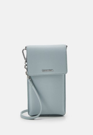 Hellblaues Calvin Klein Umhängetasche für das Handy mit Klappe, Handschlaufe und silberner Hardware auf weißem Hintergrund.