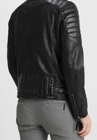 Giacca in pelle nera con dettagli trapuntati sulla schiena e sulle spalle, dotata di una cerniera laterale e di una texture liscia.