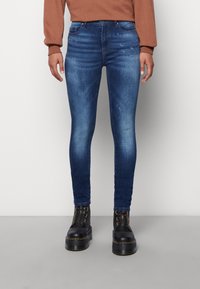 Tight jeans i mörkblå denim med en blekt textur, med fem fickor och en midjehög linning. Kombineras med svarta plattformstövlar.
