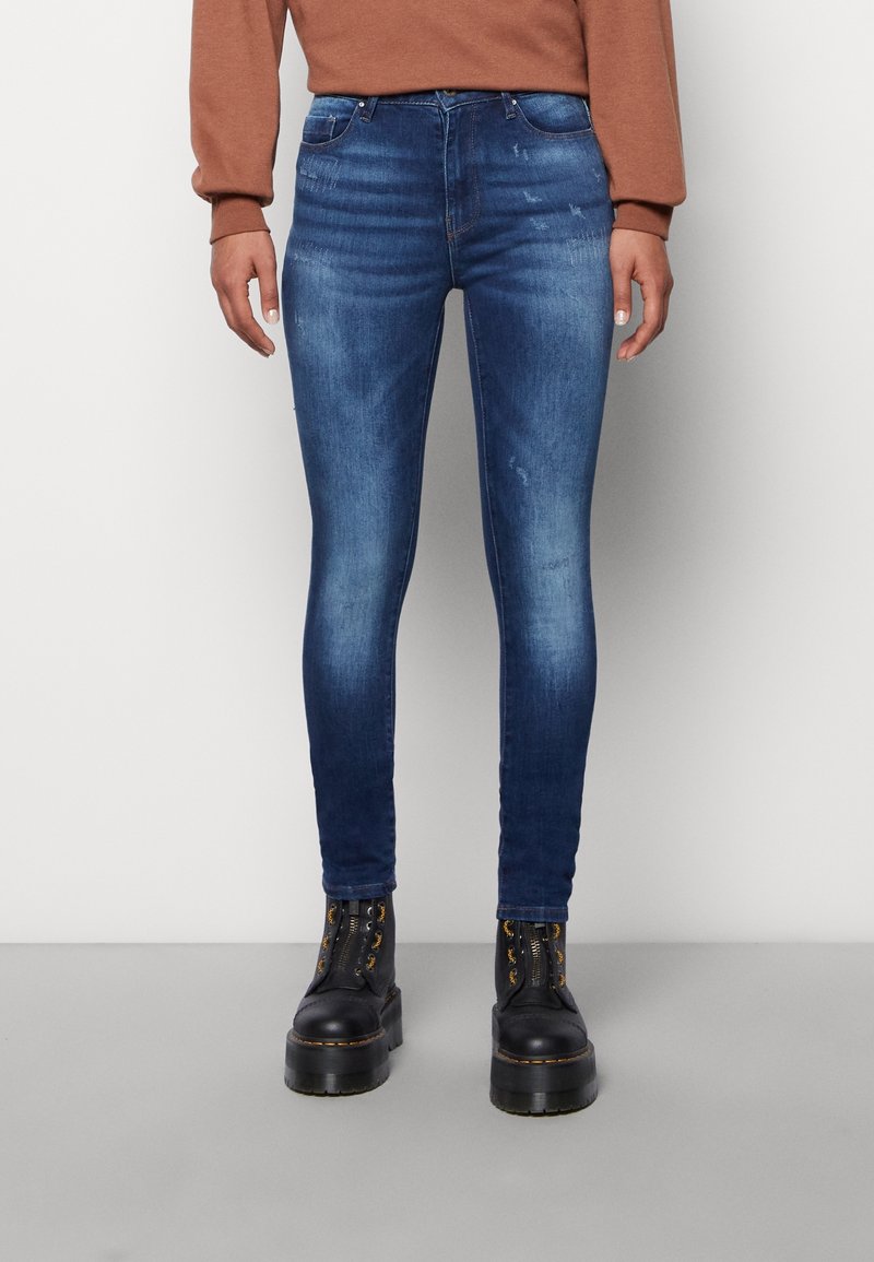 Tight jeans i mörkblå denim med en blekt textur, med fem fickor och en midjehög linning. Kombineras med svarta plattformstövlar.
